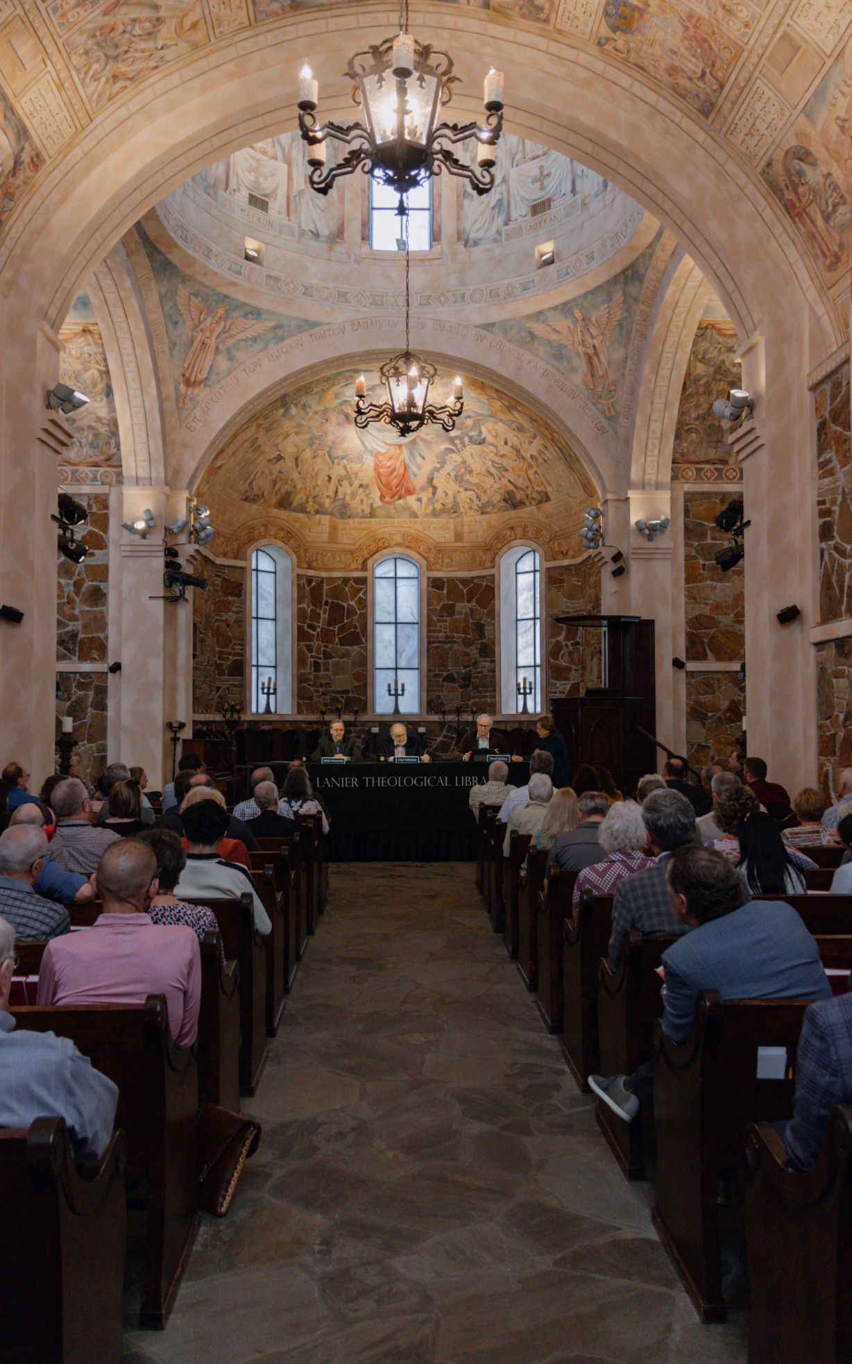 Four panelists sit at a wide table in the chapel.