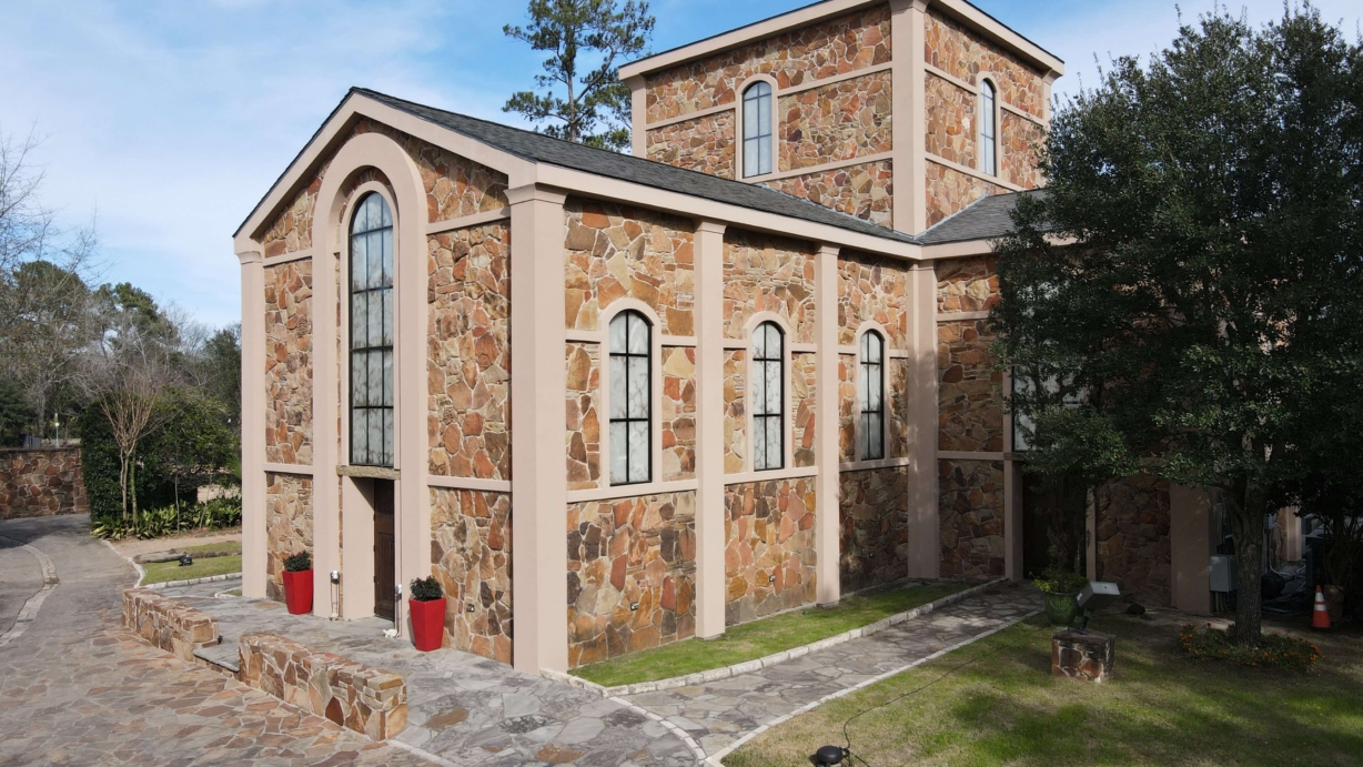 The front of the Stone Chapel. The large wood doors have images carved into them. There is a large tree to the right and grassy area.
